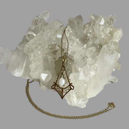 Main photo of 9kt gold opal necklace seen displayed on a rock of natural quartz crystal. The pendant with opal is in the foreground with the chain spread over the crystal and reappearing in a curve around the front of the pendant. The opal is mostly opaque with subtle play of colours within.