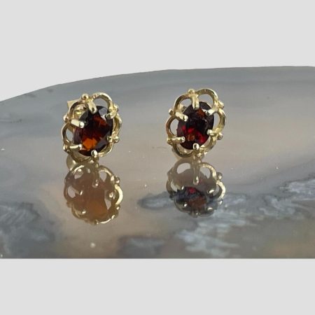 Main photo of 9kt gold &garnet studs displayed on a slice of natural agate with just the stud fronts on display (& reflected in the agate) The garnets are securely set in gold frame with an outer 6 'petal' frame with 6 claws keeping stones safe.at the front. The garnets are a beautiful shade of smoky red which compliments the gold setting perfectly.
