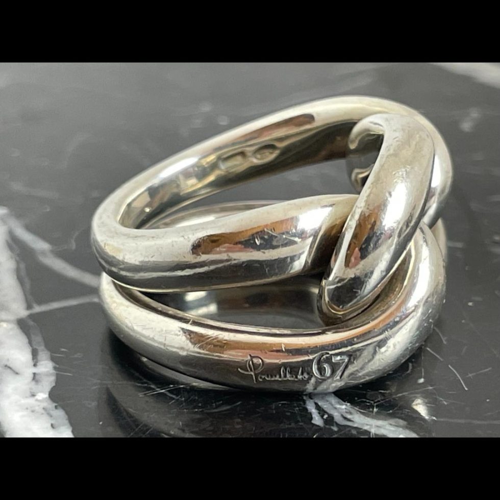 Photo of Pomellato Gourmet knot ring displayed on top of some blaack marble with the ring front facing right. The Pomellato 67 mark is visible on the outside lower band and the hallmark is just visible on the top inside band.
