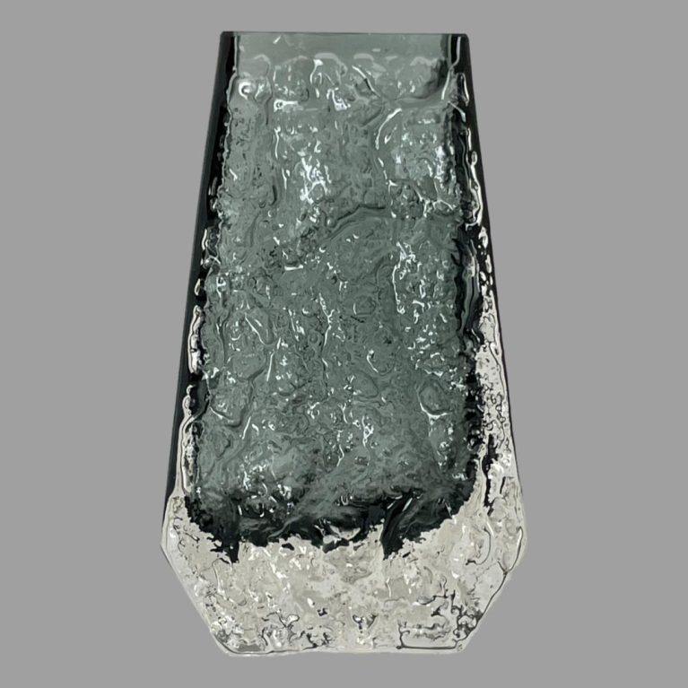 Main photo of Whitefriars 'Coffin' vase seen from an eye level with the wider side of vase on display. The lower area of the vase is clear textured glass with the rest in pewter.