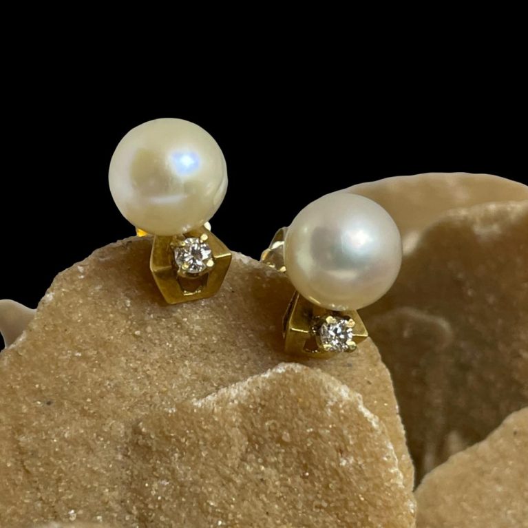 Main photo of gold pearl diamond studs displayed on a rock of natural desert sand rose with the earring fronts forward facing. the pearl is at the top and the diamond below. With the position of the posts which are central at the back, it should be possible to wear these with the diamonds at the top as well as to the side along the lobe although this positioning is probably the intended one.