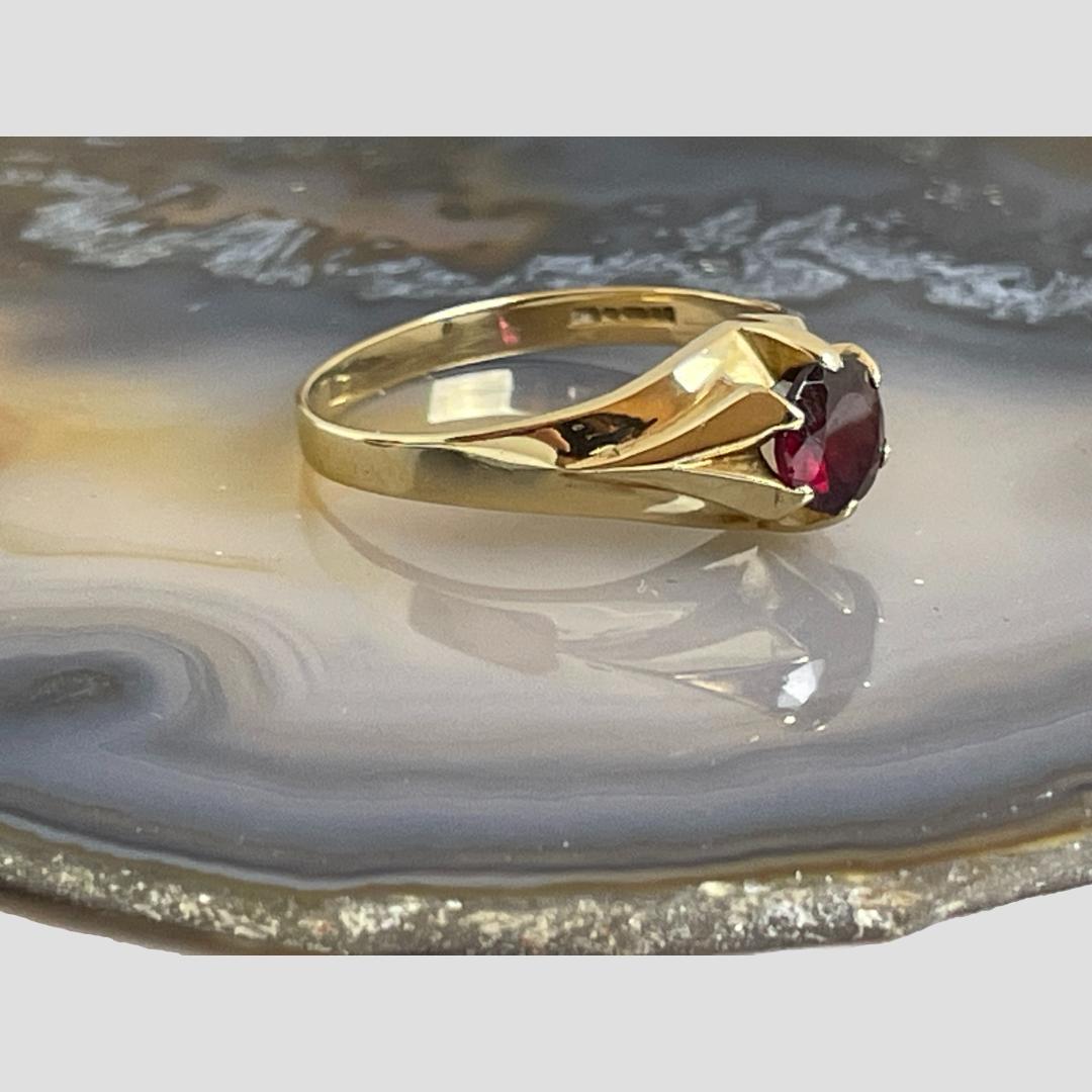 Photo of gold garnet signet ring displayed on a slice of natural agate with the ring front facing towards the right. The elevated setting for the garnet is visible.