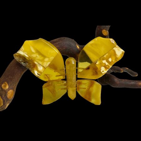 Main photo of Baltic amber butterfly brooch displayed upright leaning against a natural polished twig. The brooch is wholly put together with pieces of natural amber mostly egg yolk. This is a very eye catching and striking piece which will enhance any article of clothing or head wear.