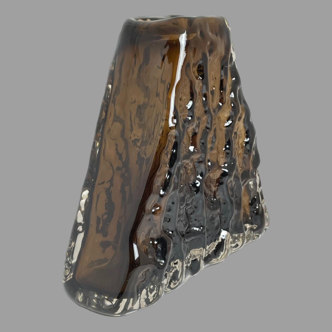Photo of Whitefriars pyramid bark vase displayed at a diagonal angle with one wide flat side facing towards the bottom right corner and one thin smooth glass side on the left.